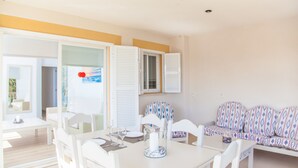 A bright, sunlit room with a dining table set for two, a sofa with patterned cushions, and a door leading to another room. - SUN OF THE BAY VIDALBA 3 (B2 - A3) - Apartment with sea views in Port d'Alcudia. Free WiFi (Alcúdia)