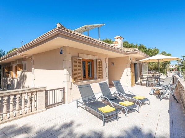 Une villa de style méditerranéen dotée d’une terrasse ensoleillée, d’un espace salon extérieur et d’un espace piscine.