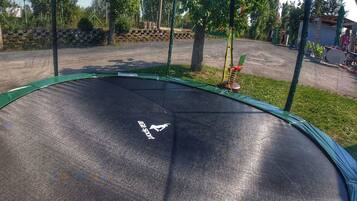 Ein Trampolin mit Sicherheitslogo, umgeben von Bäumen und einem Kiesbereich.
