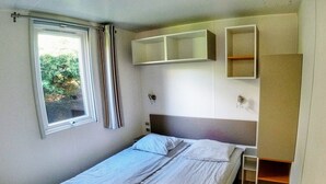 A single bed with a headboard, a window with curtains, and built-in shelving above the bed.
