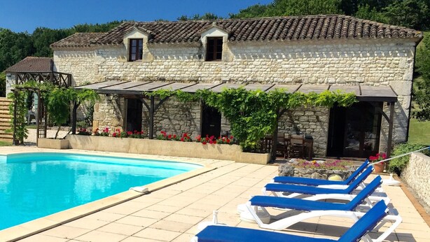 A stone building with a pool and lounge chairs.