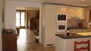 A kitchen with white cabinets, a stove, and a microwave. There is a wooden staircase leading to another room.