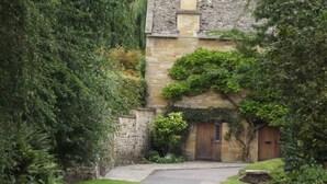 A narrow stone pathway leading to a traditional stone building with a wooden door, surrounded by lush greenery. - Cornerstone Cottage -  a cotswold cottage that sleeps 2 guests  in 1 bedroom (Chipping Campden)
