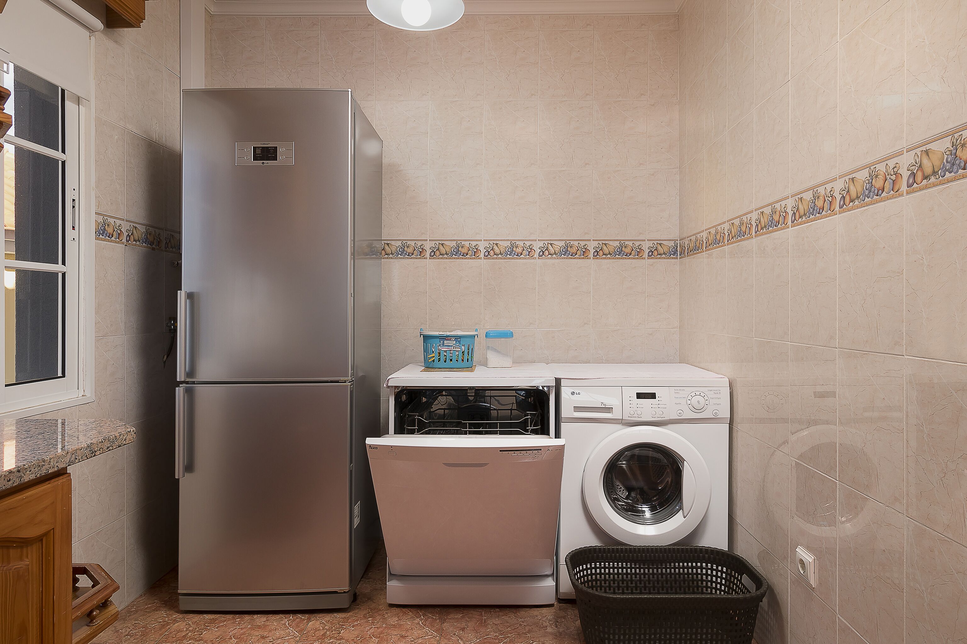 A compact kitchen with a stainless steel refrigerator, a dishwasher, and a washing machine.