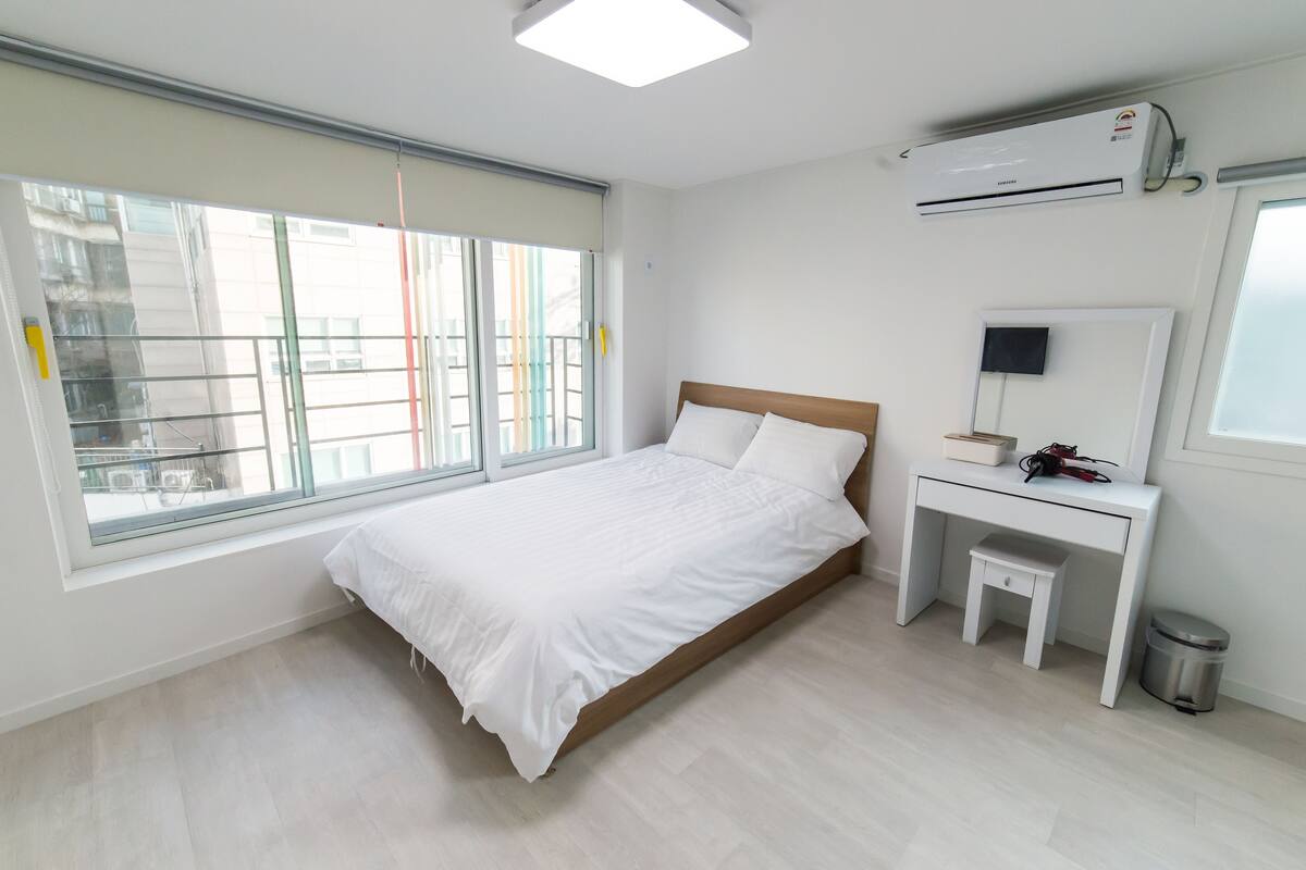 Une chambre d’hôtel moderne dotée d’une grande fenêtre, d’un lit, d’un bureau avec une chaise et d’un appareil de climatisation.
