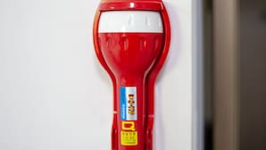A red fire extinguisher mounted on a white wall. - Kpop Haus (Seoul)
