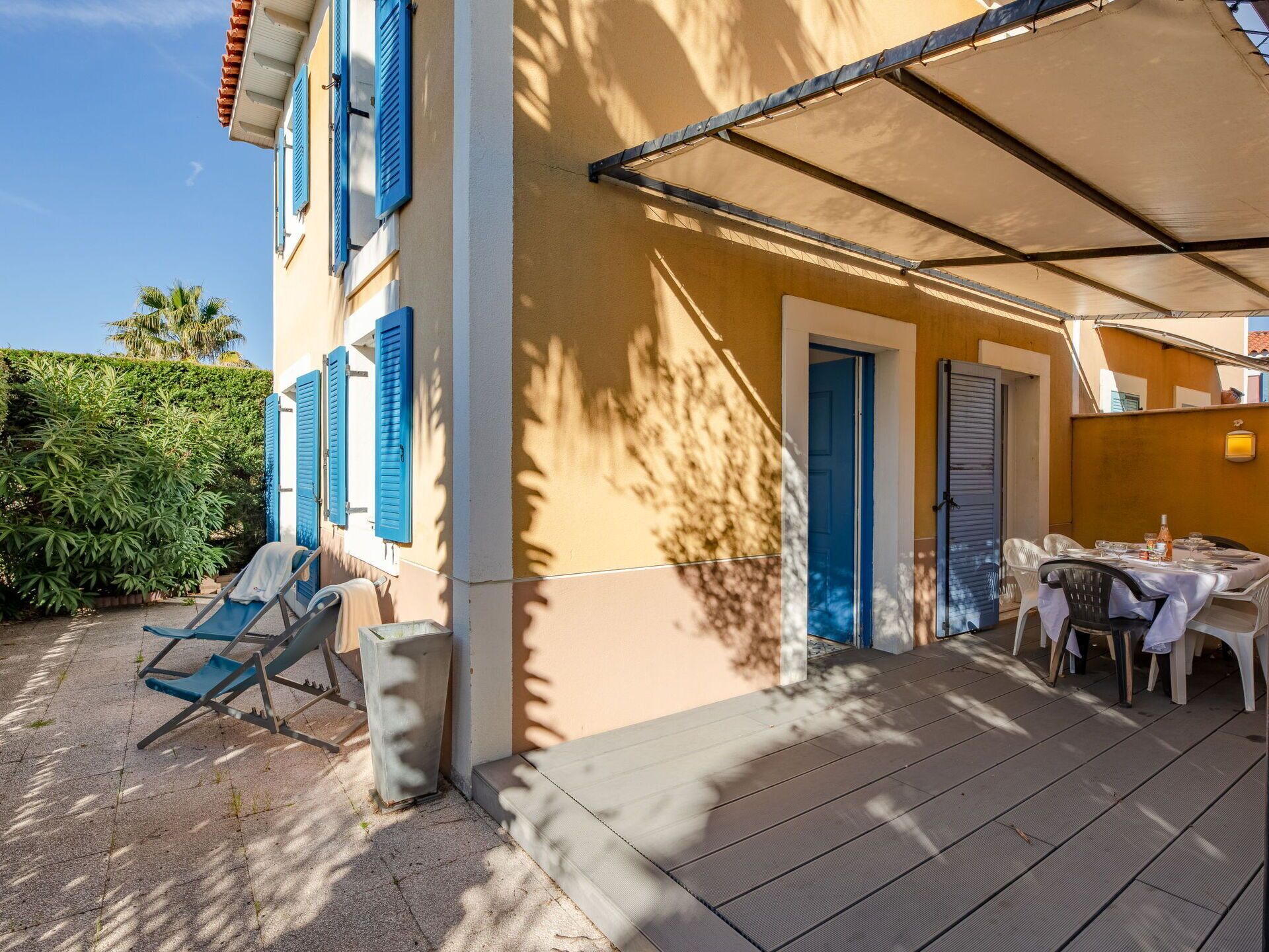 A covered outdoor seating area with a table and chairs, a door, and a small trash bin.