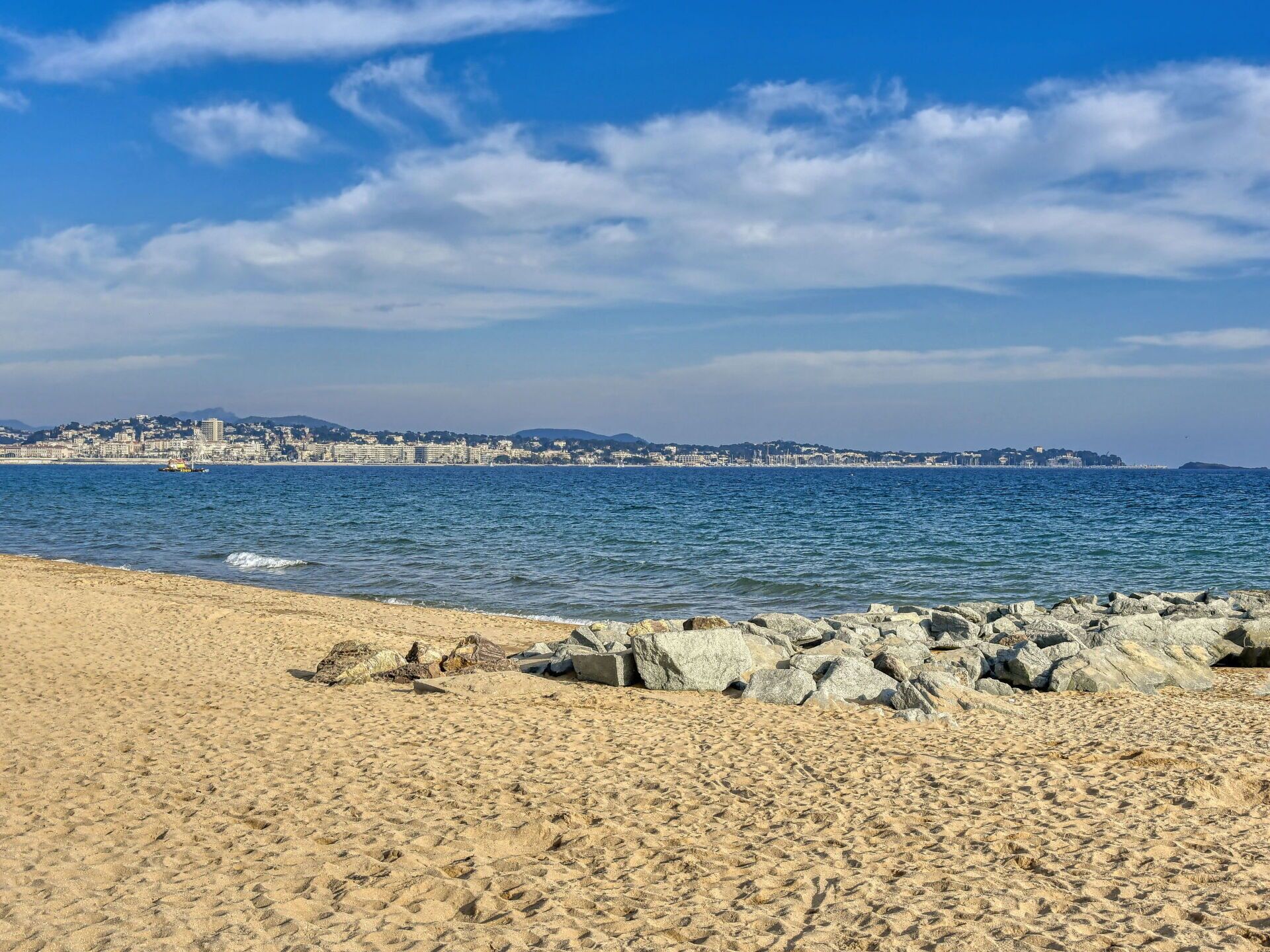 A beach with a rocky shoreline and a distant cityscape.