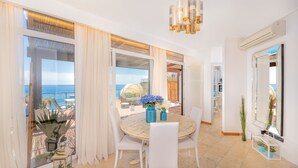 Un comedor con una mesa redonda, sillas blancas y vistas al mar a través de amplios ventanales.