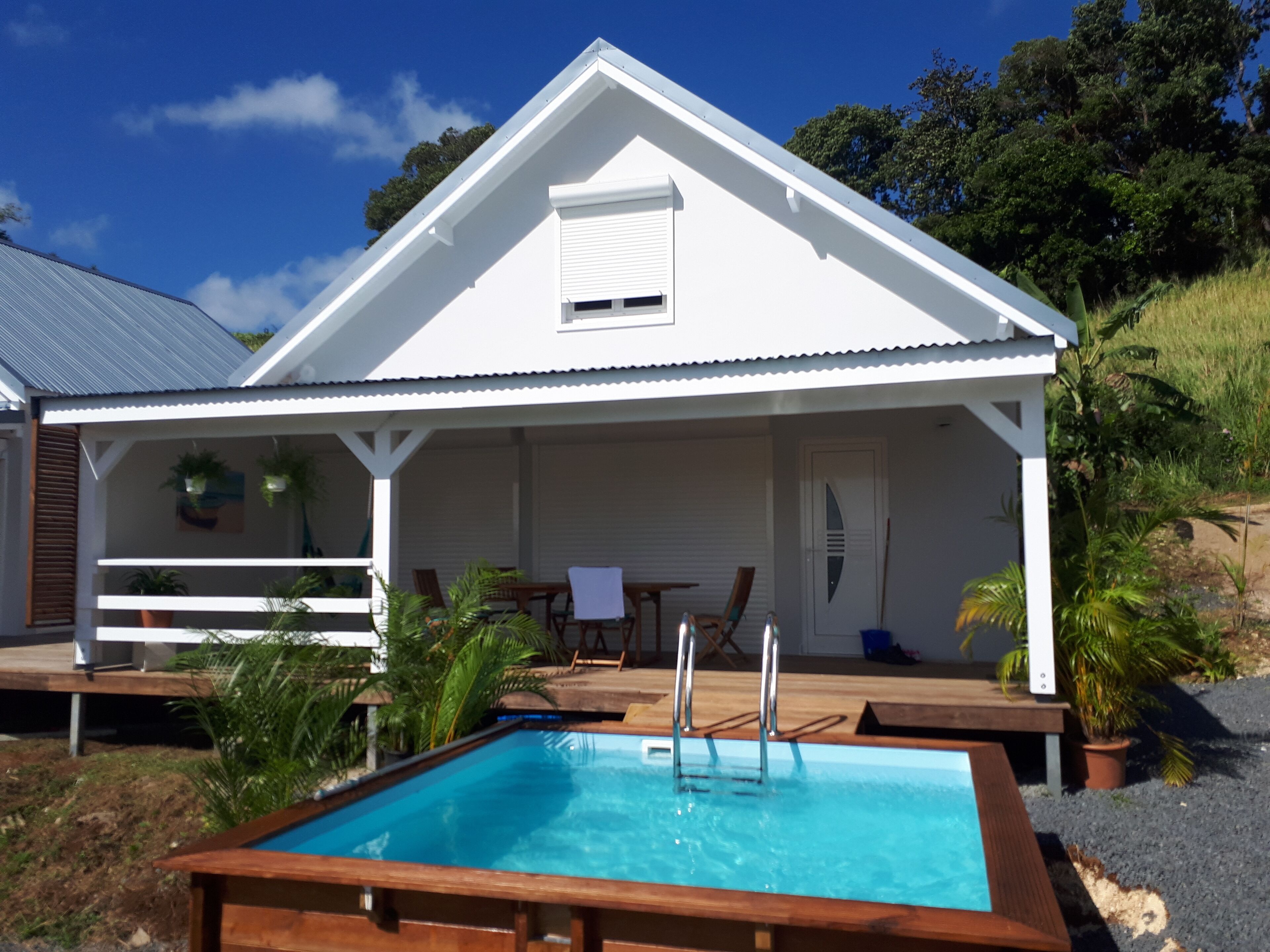 A white building with a covered patio, a pool, and outdoor seating.