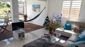 Una sala de estar moderna con un televisor de pantalla plana, una mesa de centro de vidrio, un sofá y una hamaca.