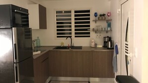 Cocina compacta con horno integrado, lavamanos y ventana con persianas.