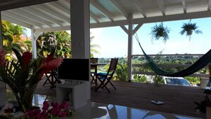 Un espacio al aire libre techado con mesa de vidrio, sillas y una hamaca.