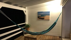 Una hamaca en una terraza de madera con una planta en maceta y un cuadro de un bote en la playa.