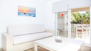A modern living room with a white sofa, a coffee table, and a painting of a sunset over the ocean. - SUN OF THE BAY 3 (B3 - A3) - Apartment with sea views in Port d'Alcúdia. Free WiFi (Alcúdia)
