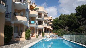 Une piscine entourée de chaises longues, un sentier en pierre et des immeubles à plusieurs étages dotés de balcons.
