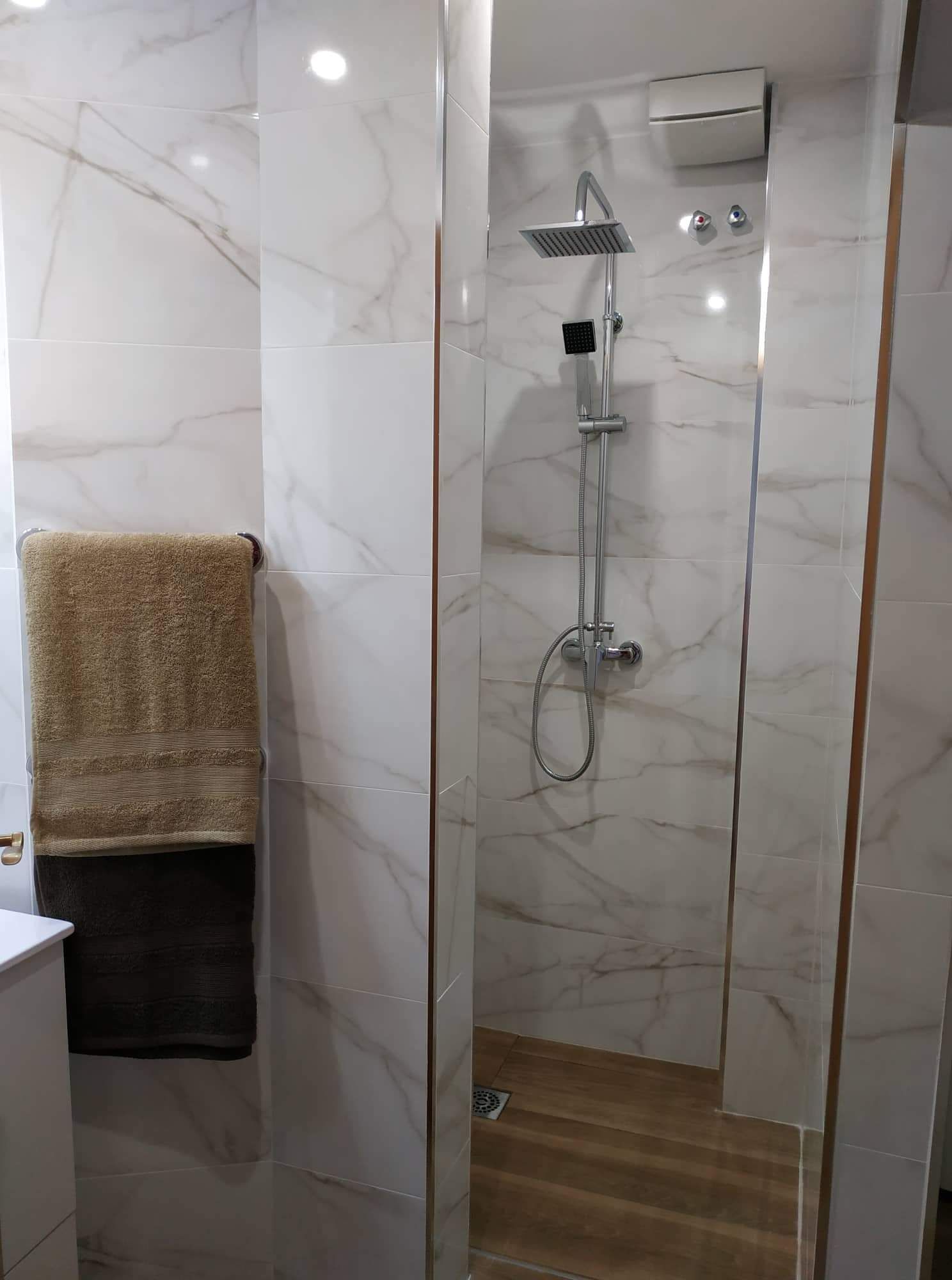Un baño moderno con cabina de ducha de vidrio, paredes de mármol y suelo de madera.