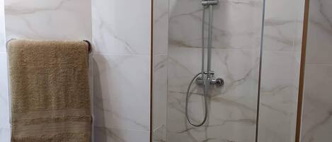 Un baño moderno con cabina de ducha de vidrio, paredes de mármol y suelo de madera.