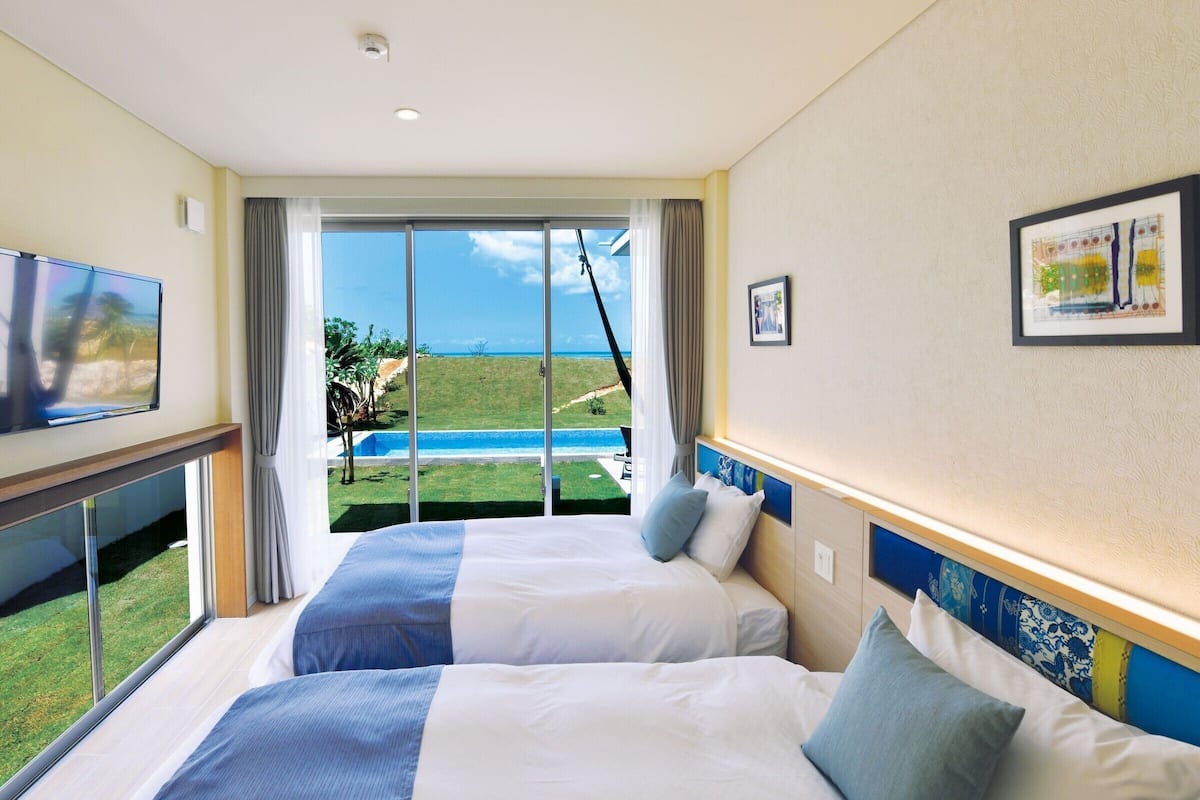 Ett hotellrum med två sängar, en TV, ett stort fönster med utsikt över havet och en säkerhetskamera som är monterad i taket.