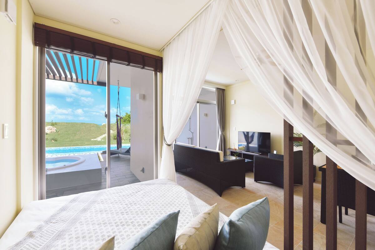 Een slaapkamer met een bed, een televisie en uitzicht op een zwembad en het landschap.