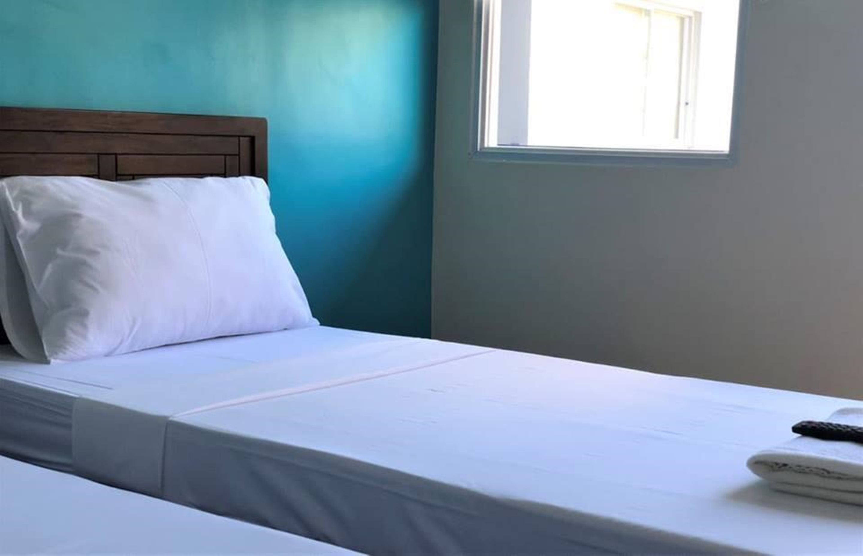 A single bed with a wooden headboard, a white pillow, and a remote control on the bed.