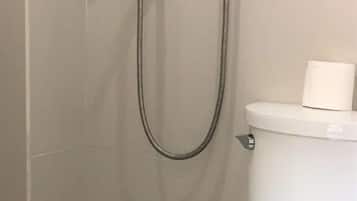 A small, enclosed shower area with a toilet and a towel dispenser.