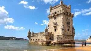 A historic stone tower with a balcony, overlooking a body of water.