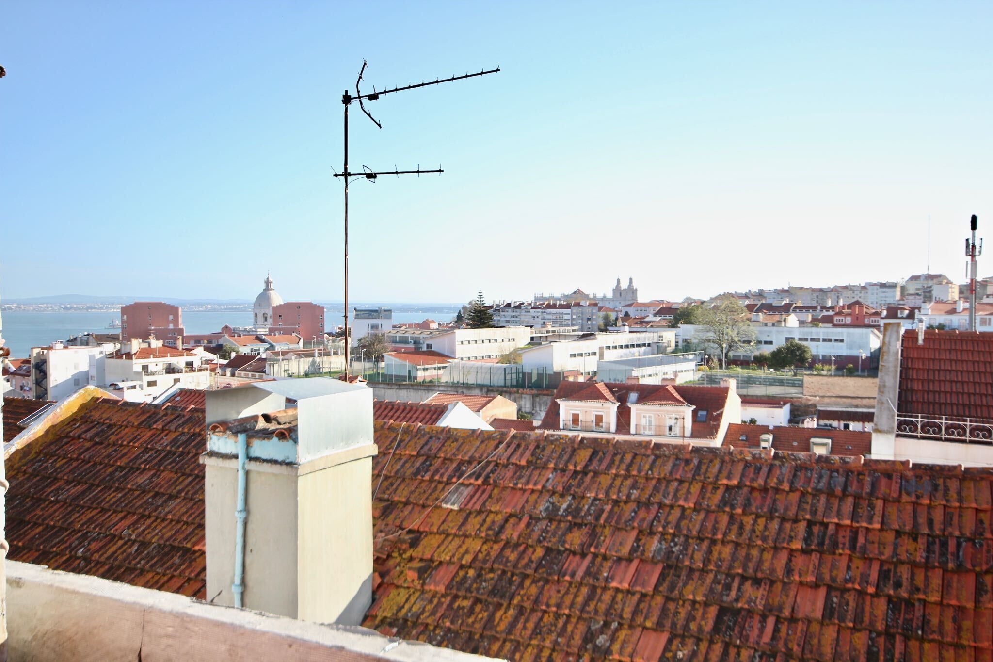 Eine Stadtansicht mit roten Ziegeldächern, einer markanten Antenne und Gebäuden im Hintergrund.