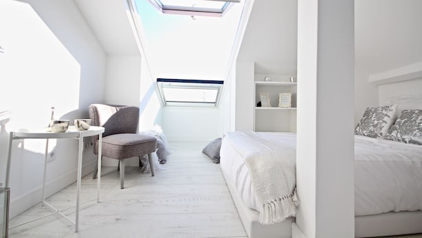 A bedroom with a skylight, a bed, a chair, and a small table.