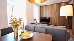 A modern living room with a sofa set, a flat-screen TV, and a dining table with a vase of flowers.