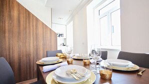 A dining table set with white plates, gold cutlery, and glasses, with a wooden panel wall and a window in the background.