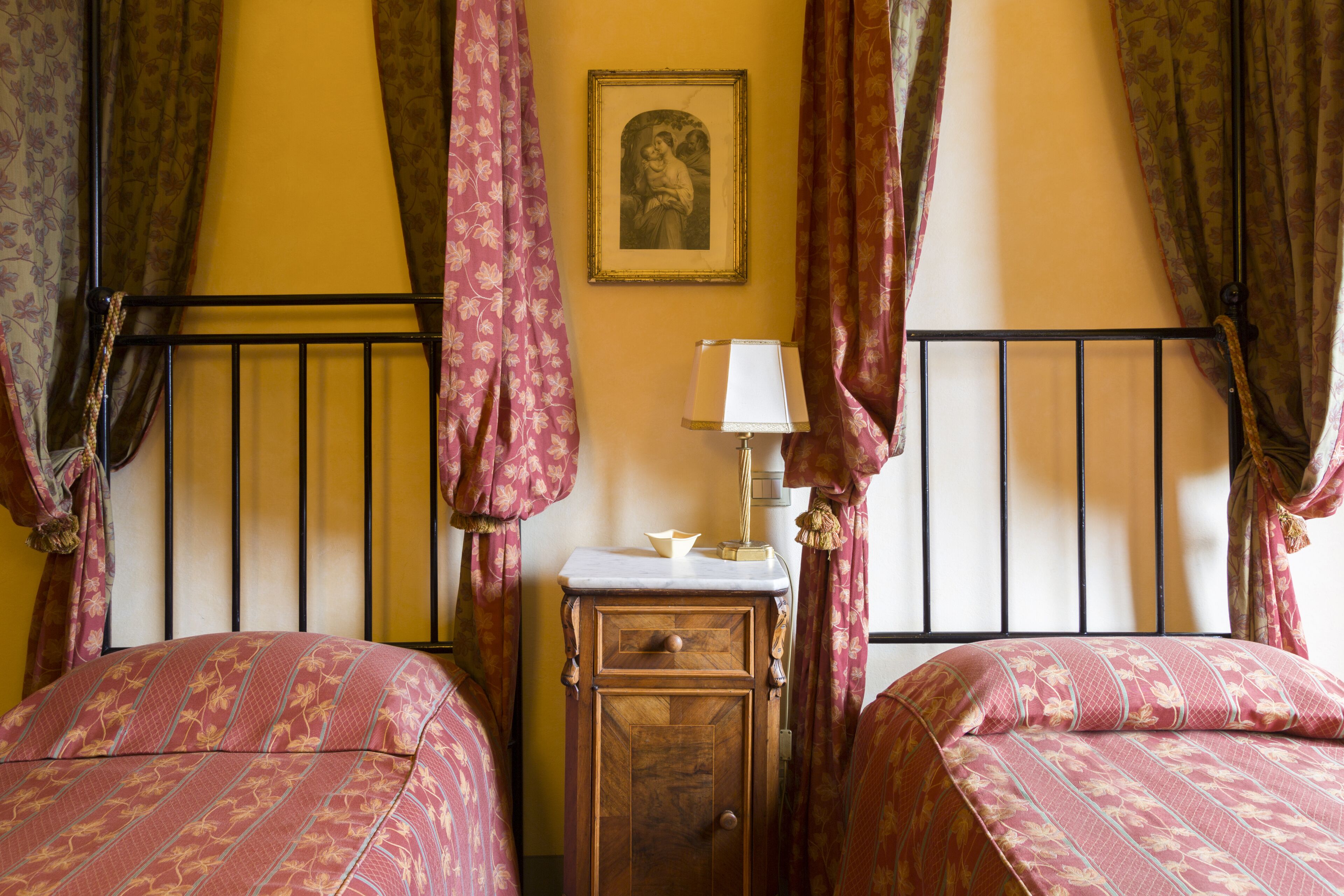 Quarto com duas camas, uma mesinha de cabeceira com abajur e um quadro na parede.