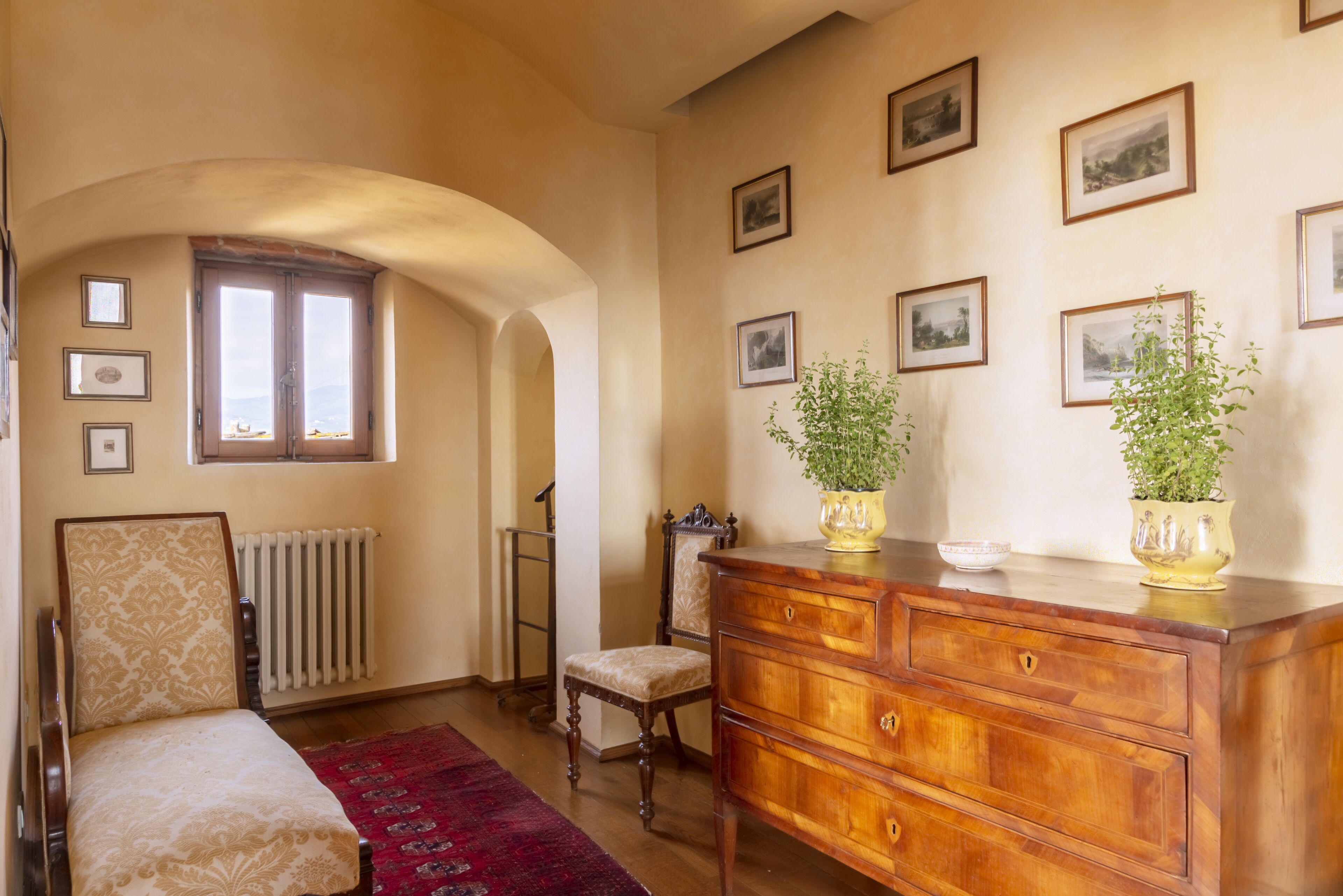 Une pièce comprenant une commode en bois, une chaise, un radiateur et des tableaux encadrés accrochés au mur.