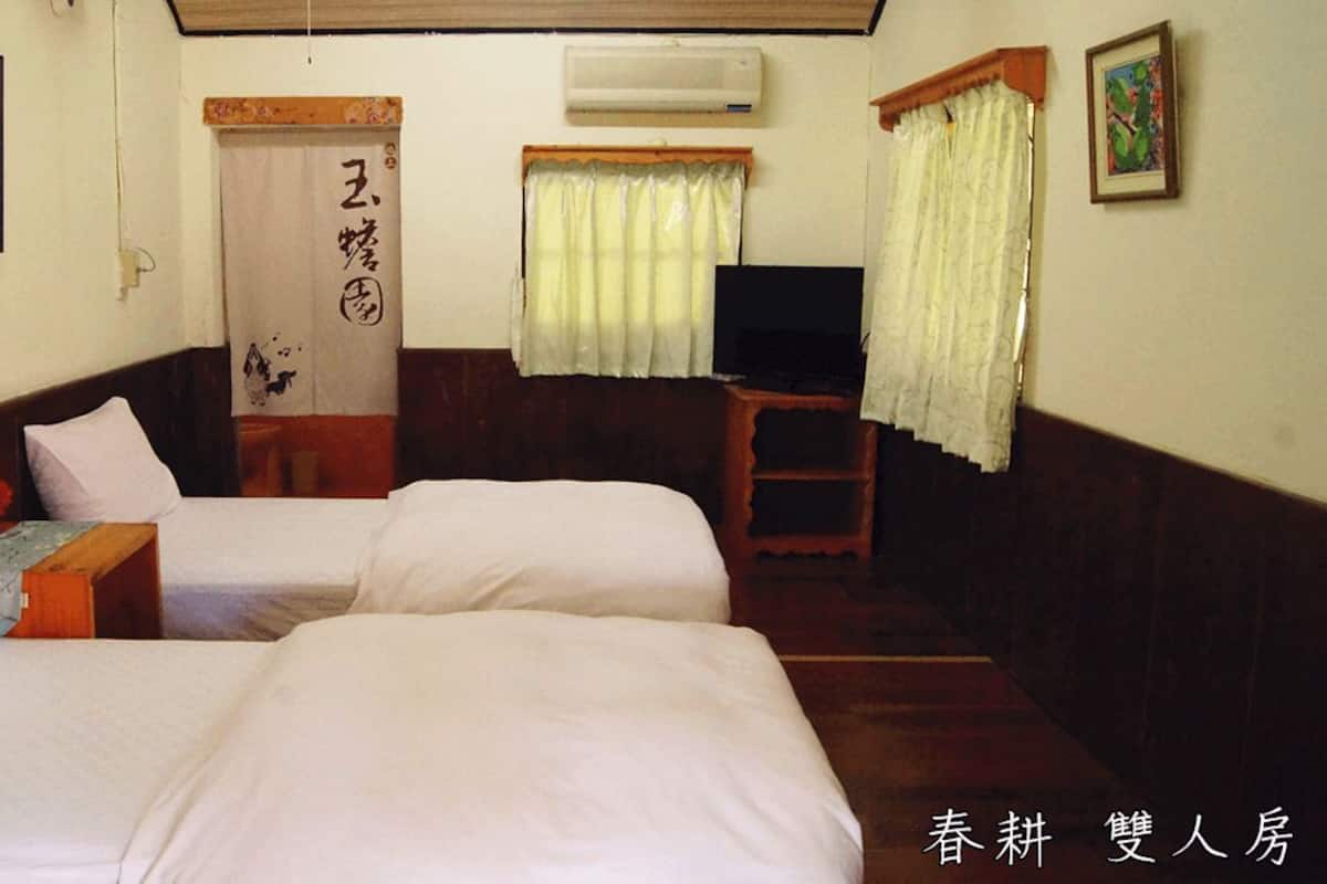 A room with two beds, a wooden headboard, a small table, a TV, and a curtain.