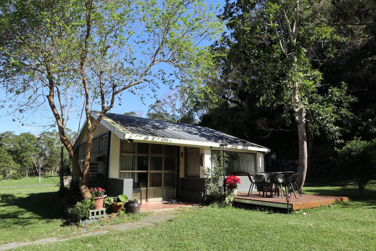 A small house with a porch, surrounded by greenery and trees.