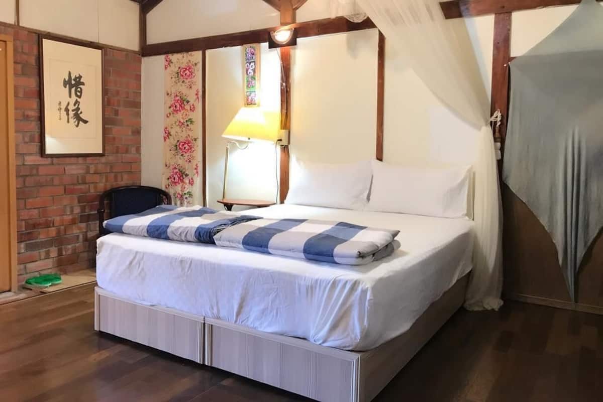 A bedroom with a bed, a nightstand, a lamp, a framed picture, and a window with curtains.