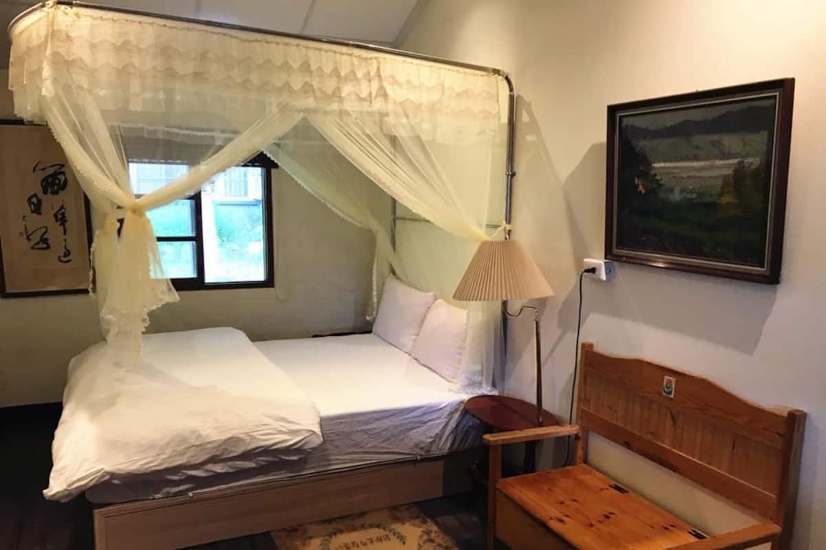 A room with a bed under a canopy, a wooden bench, a lamp, and a painting on the wall.