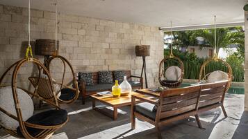 Un espacio exterior acogedor con sillas de mimbre y un banco de madera, una mesa con un jarrón y una lámpara de mimbre.