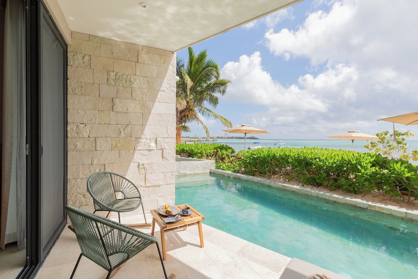 A poolside area with a view of the ocean, a chair, a table with a plate of food, and a palm tree.