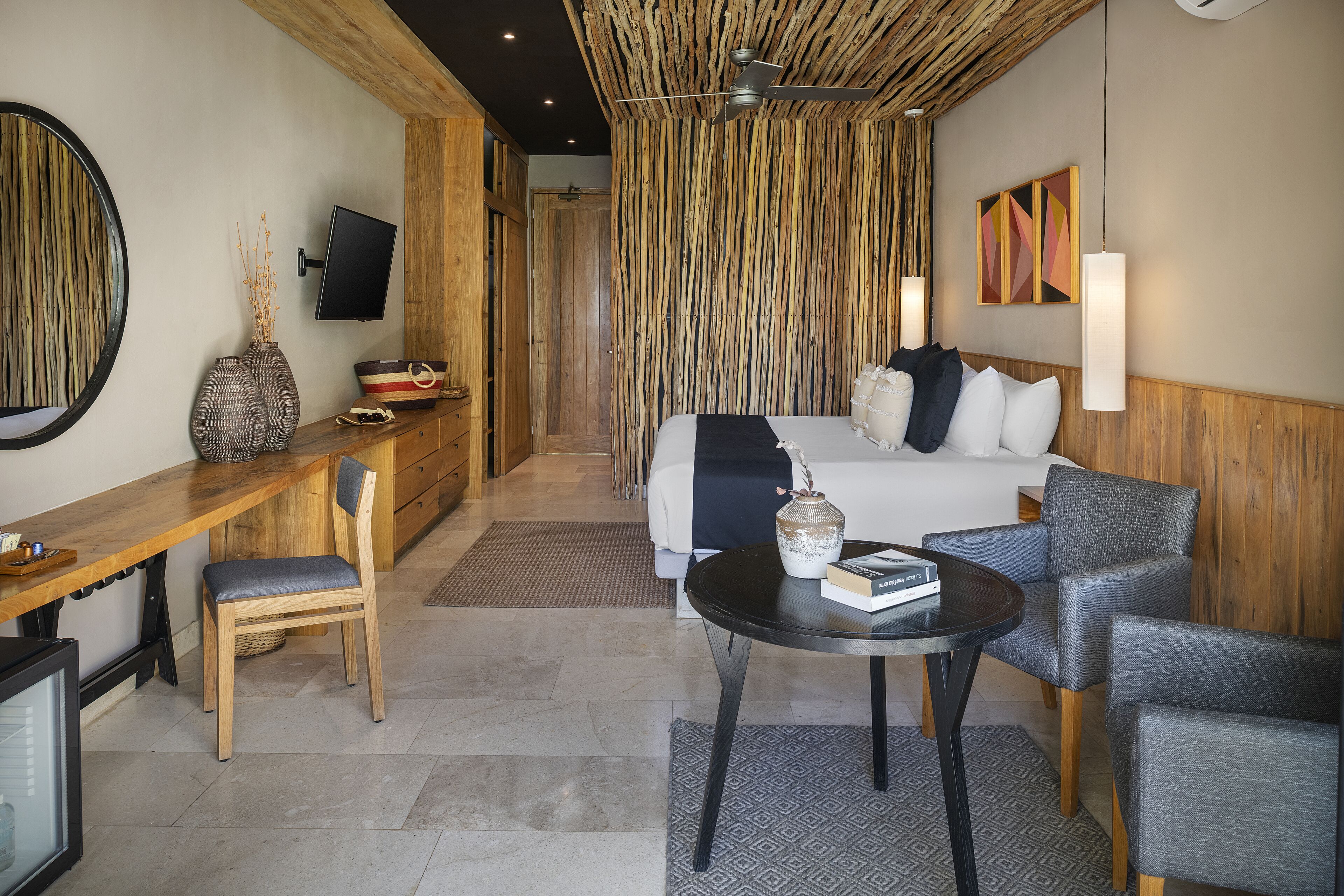 A hotel room with a bed, a desk, a chair, a TV, and a wall-mounted artwork.