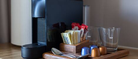 A coffee maker, a wooden tray with cups, a spoon, and packets of sugar and creamer on a wooden surface.