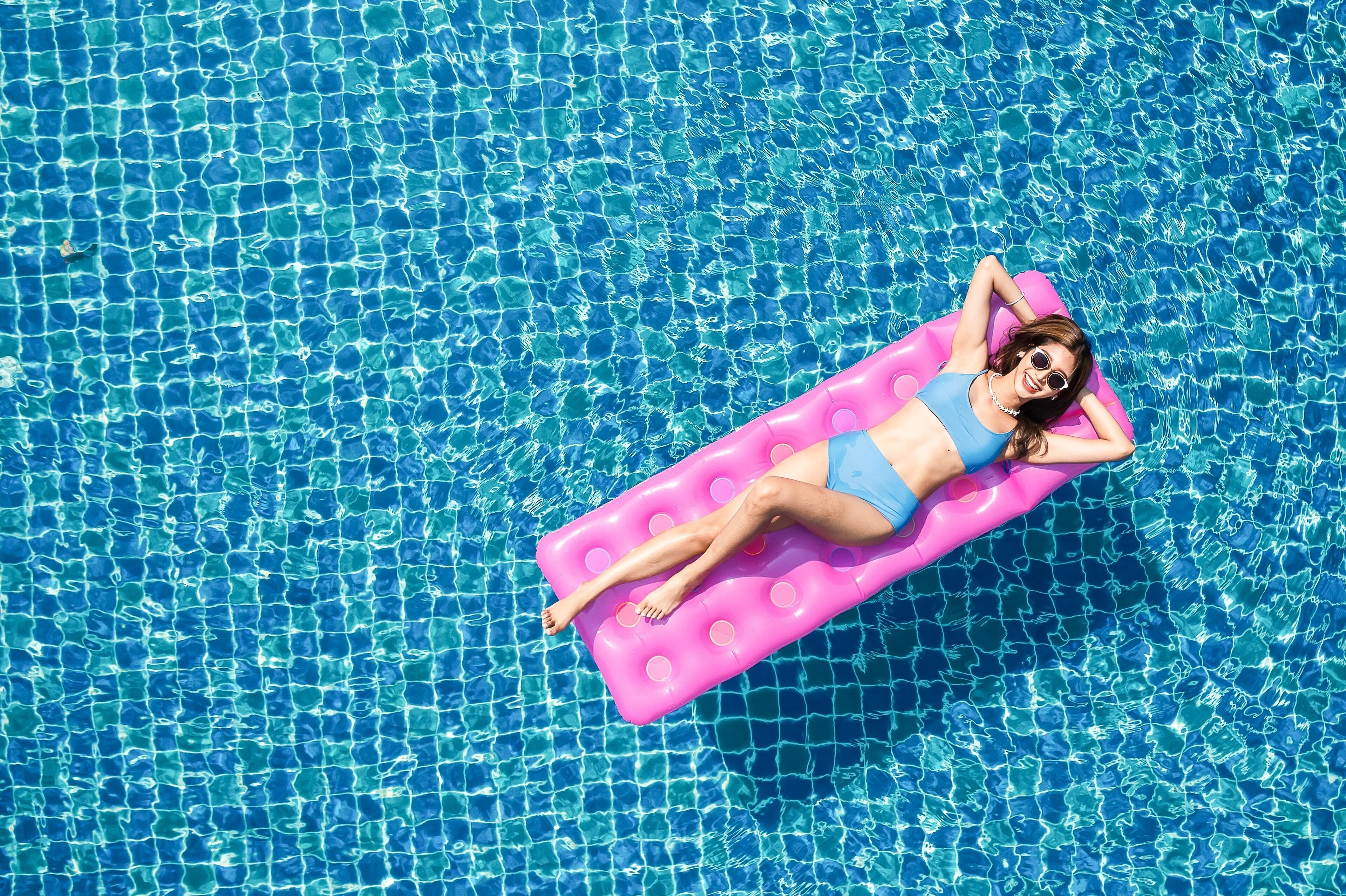 Una persona recostada sobre un flotador rosa en una piscina azul cristalina.