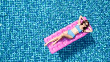 Una persona recostada sobre un flotador rosa en una piscina azul cristalina.