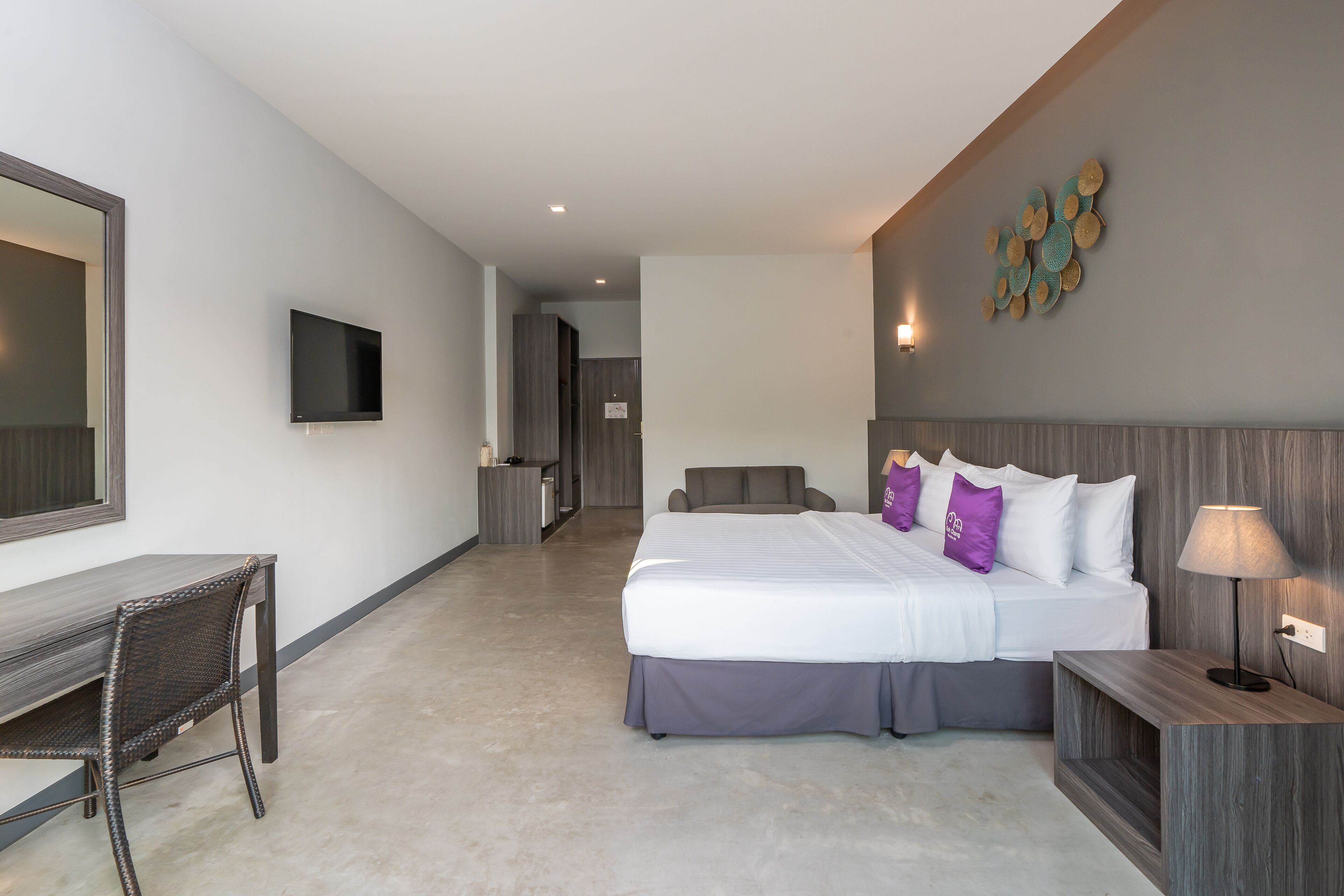 A modern hotel room with a large bed, a desk, a chair, a TV, and a wall-mounted artwork.