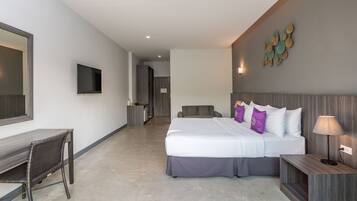 A modern hotel room with a large bed, a desk, a chair, a TV, and a wall-mounted artwork.