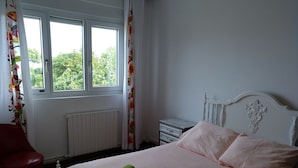 Quarto com cama, mesa de cabeceira, cadeira e janela com cortinas.