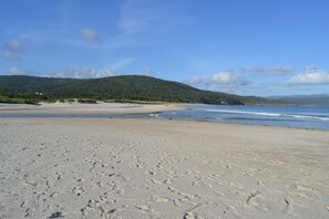 A wide sandy beach with footprints, a clear sky, and distant hills. - House with direct access to Finisterre beach (Finisterre)