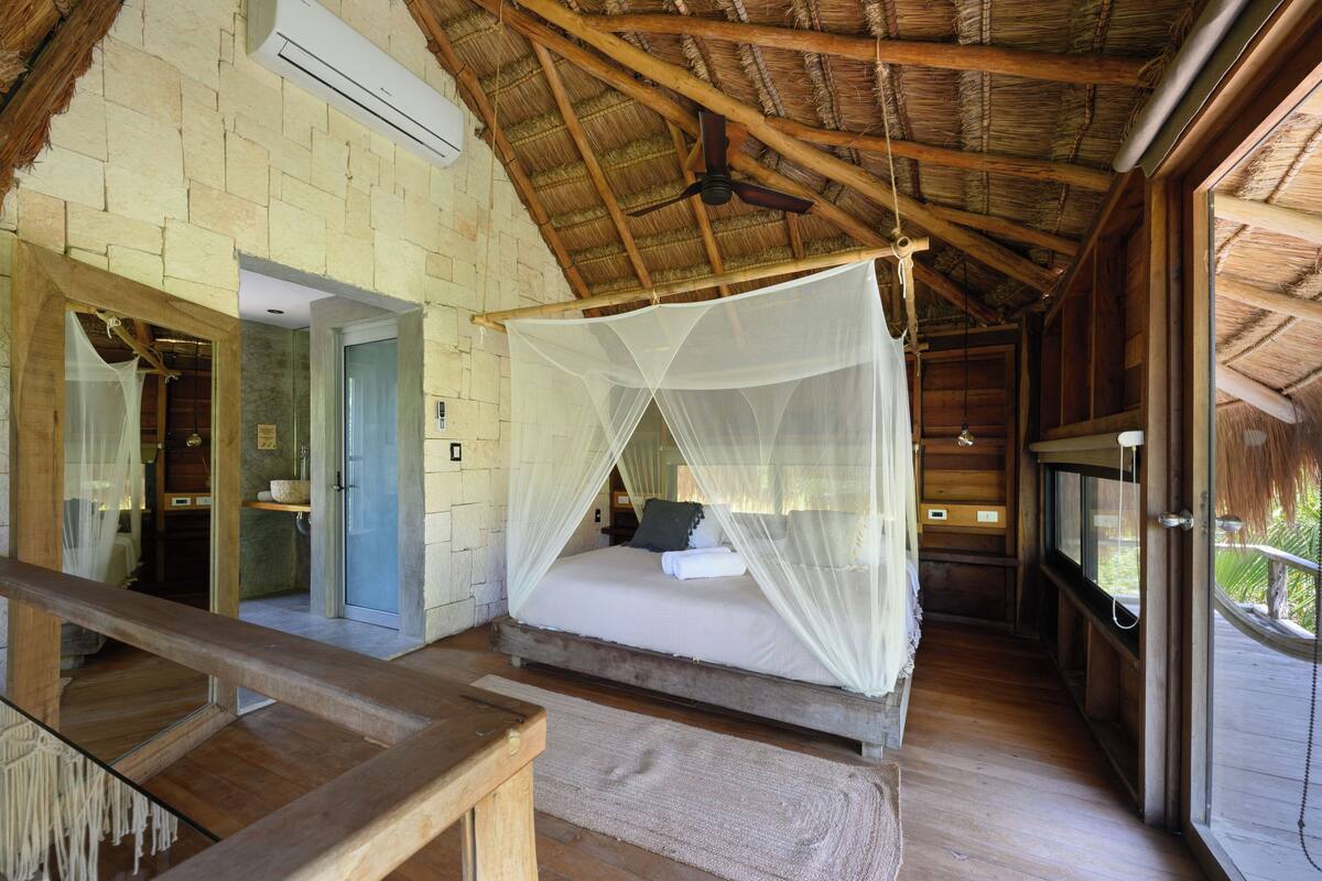 A room with a bed under a canopy, a wooden ceiling, and a view of the outdoors.