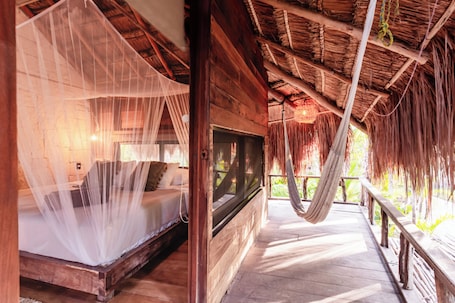 A wooden room with a bed under a mosquito net, a TV, and a hammock.