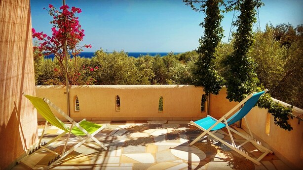 Une terrasse avec deux fauteuils de jardin, un sol carrelé et une vue sur la mer.
